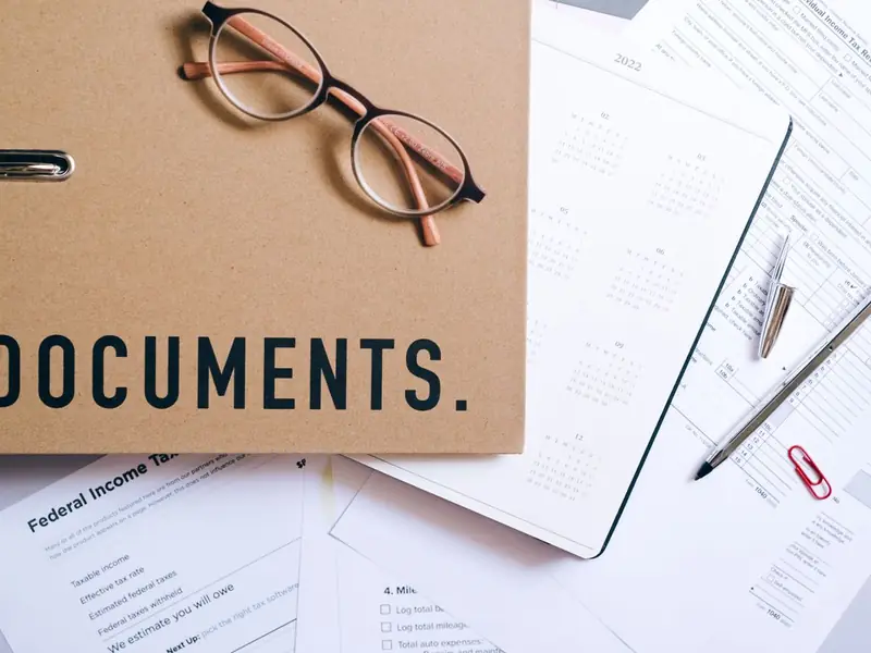 A brown folder labelled Documents with glasses, a pen and loose paperwork on a desk