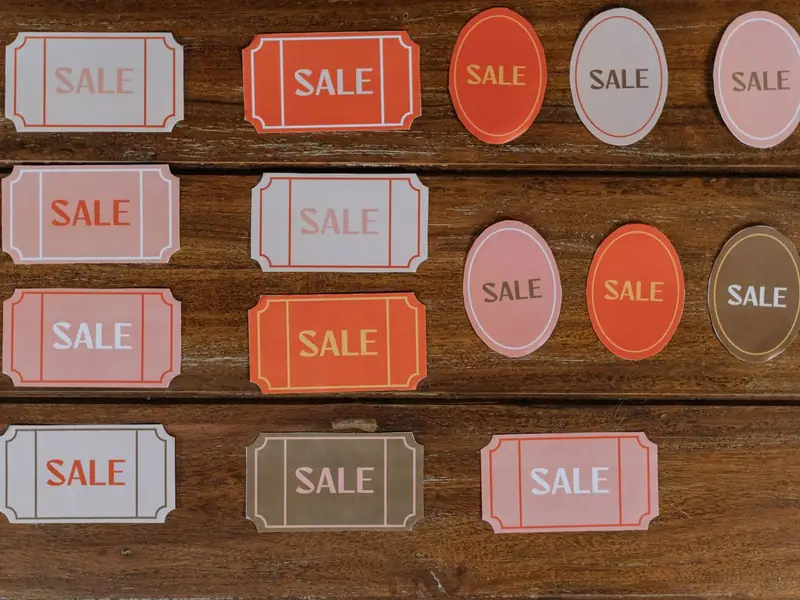 Paper sale tags in orange, pink and grey laid out on a wooden table