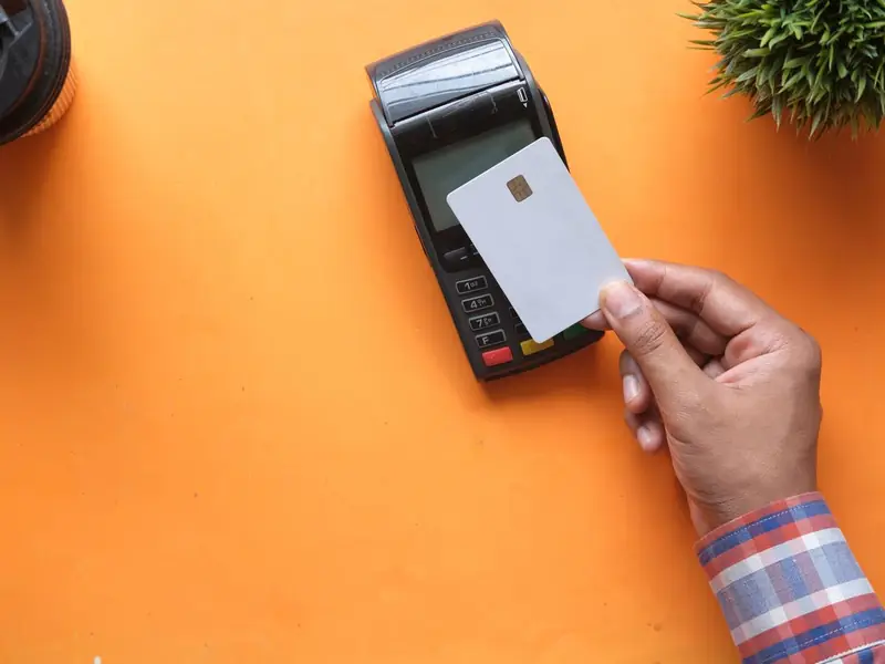 A hand holding a blank card to a card payment terminal on an orange table